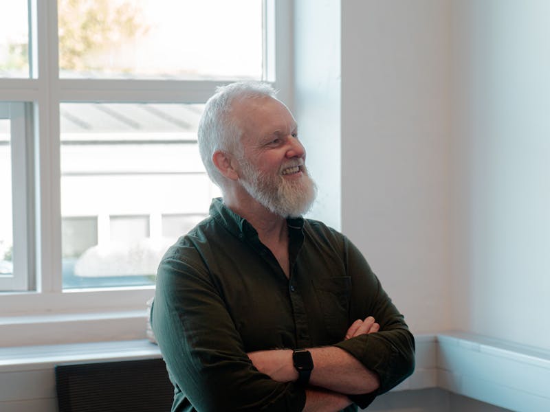 A smiling man with a white beard and crossed arms in an office setting for ServiceNow partner Adeno.