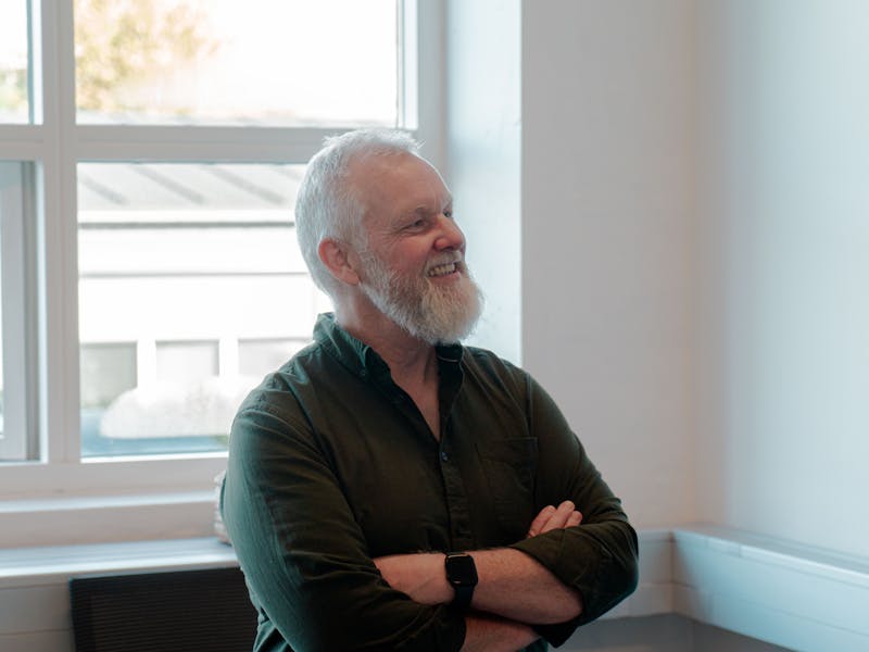 A smiling man with a white beard and crossed arms in an office setting for ServiceNow partner Adeno.