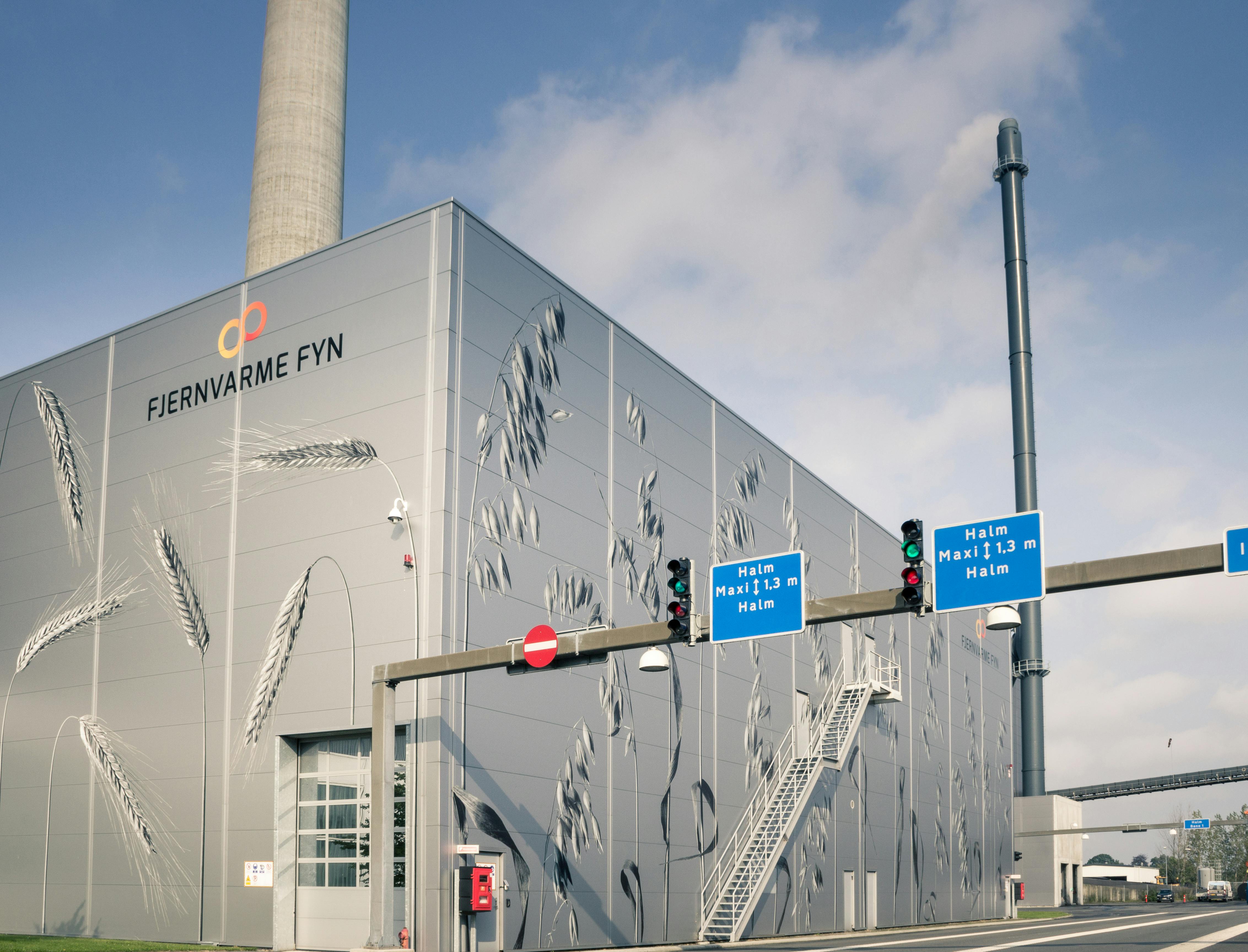 Exterior view of the Fjernvarme Fyn straw-fired power plant building with grain illustrations on the facade, highlighting a ServiceNow implementation.
