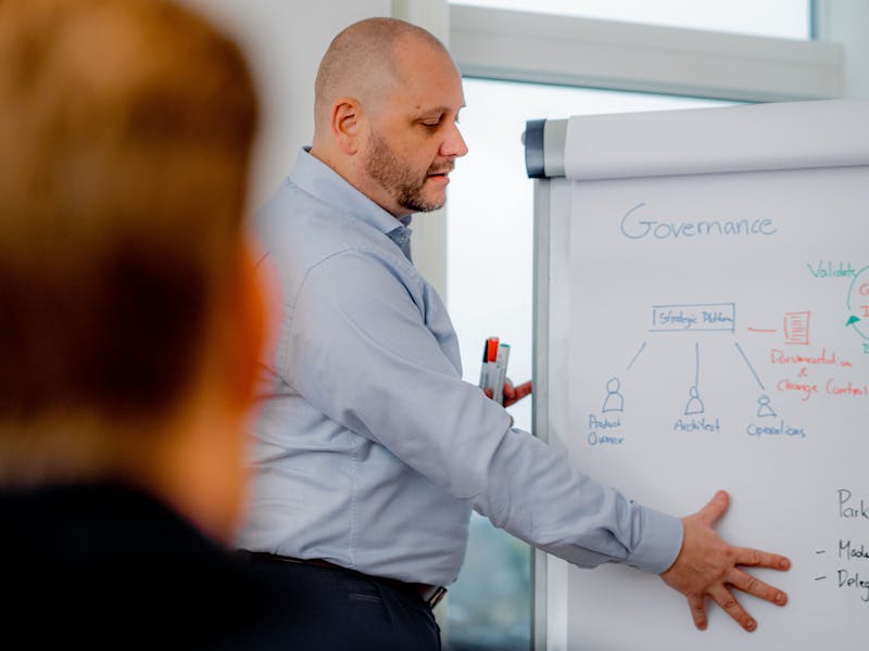 A man presenting a governance and strategic platform diagram on a whiteboard during a ServiceNow workshop.
