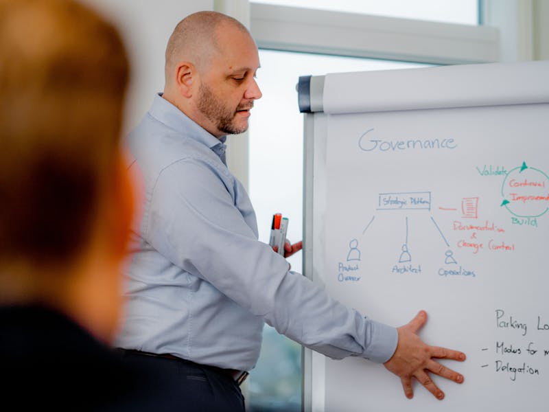 A man presenting a governance and strategic platform diagram on a whiteboard during a ServiceNow workshop.