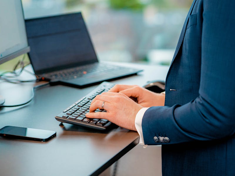 A person in a blue suit typing on a keyboard at a desk with a monitor and laptop, representing a ServiceNow professional.