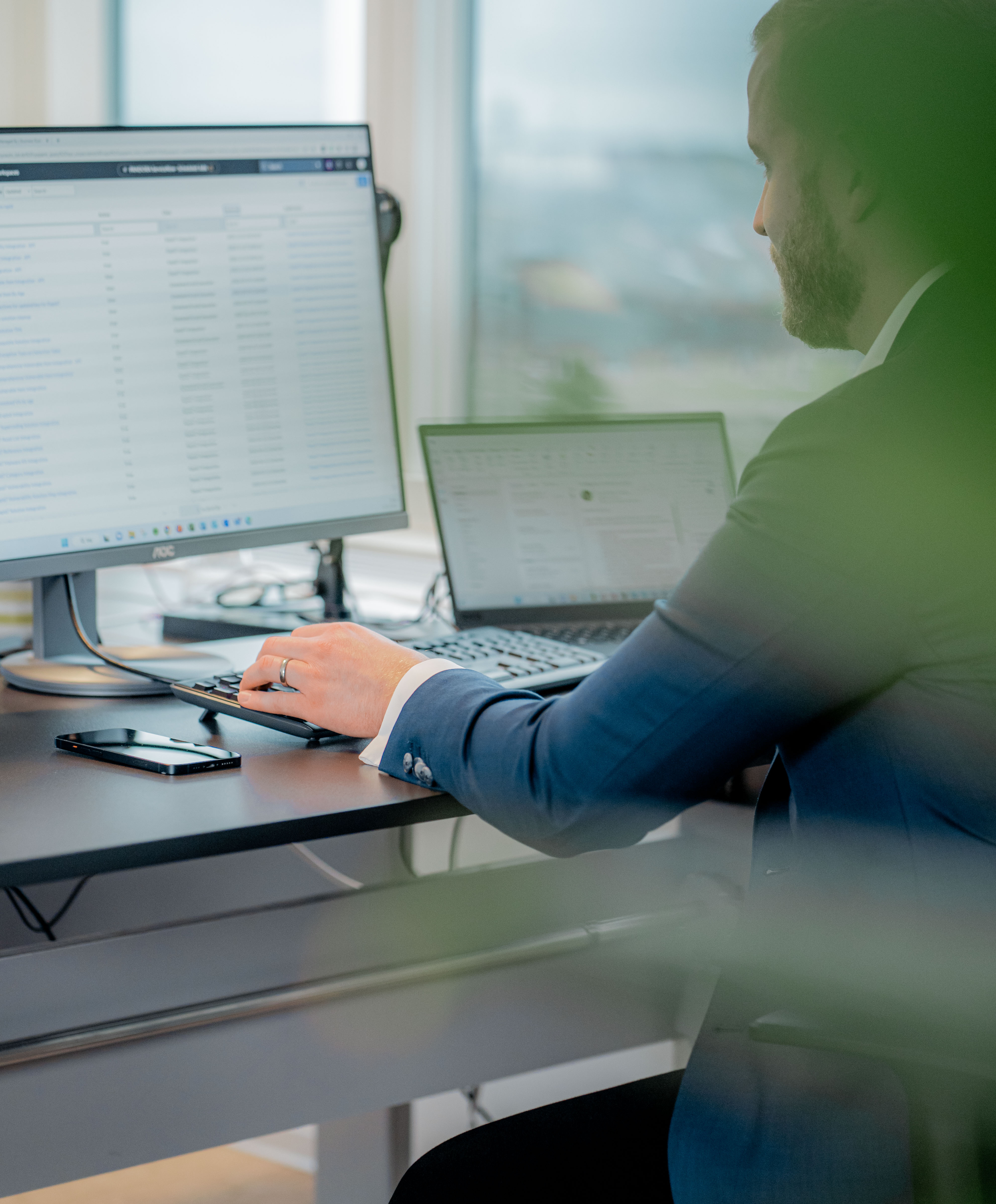 A person in a suit working at a desk with a computer monitor displaying a ServiceNow interface.