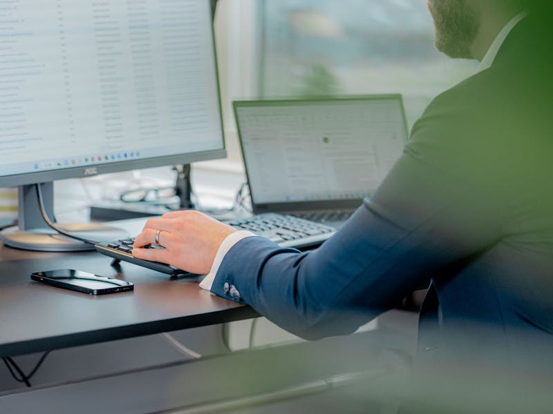 A person in a suit working at a desk with a computer monitor displaying a ServiceNow interface.
