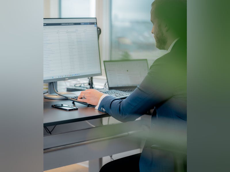 A person in a suit working at a desk with a computer monitor displaying a ServiceNow interface.