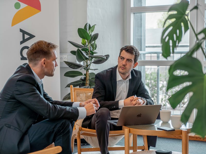 Two men in business suits having a discussion in an office for ServiceNow partner Adeno.