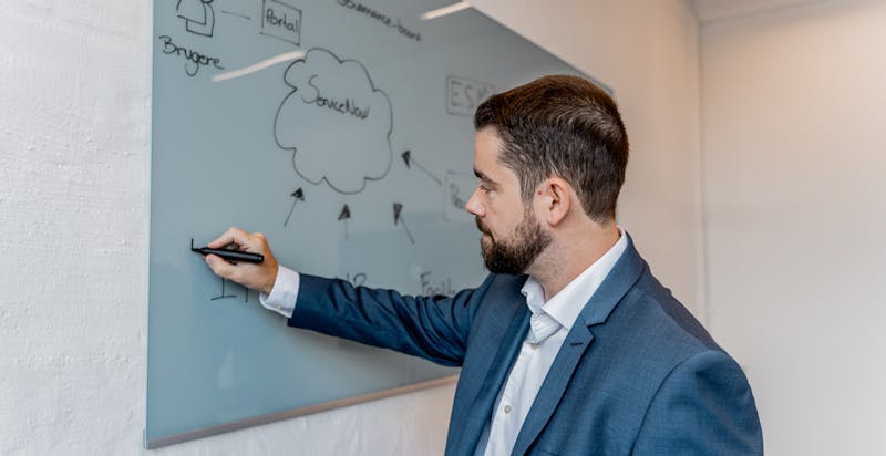 A man in a suit writing on a glass whiteboard featuring a ServiceNow cloud diagram.