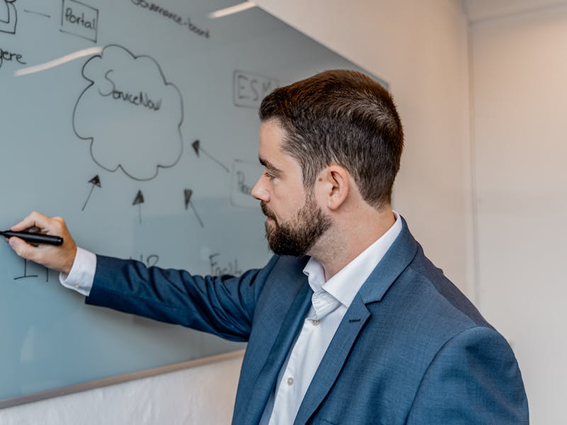 A man in a suit writing on a glass whiteboard featuring a ServiceNow cloud diagram.