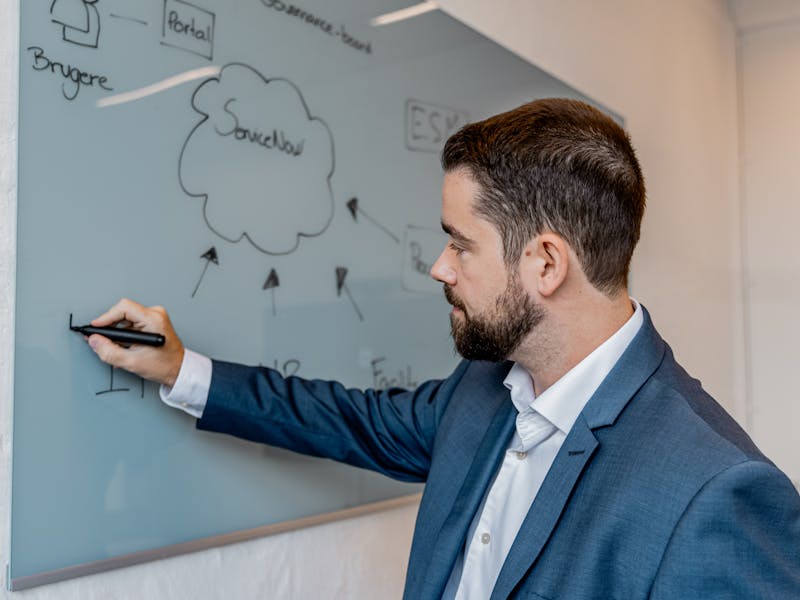 A man in a suit writing on a glass whiteboard featuring a ServiceNow cloud diagram.
