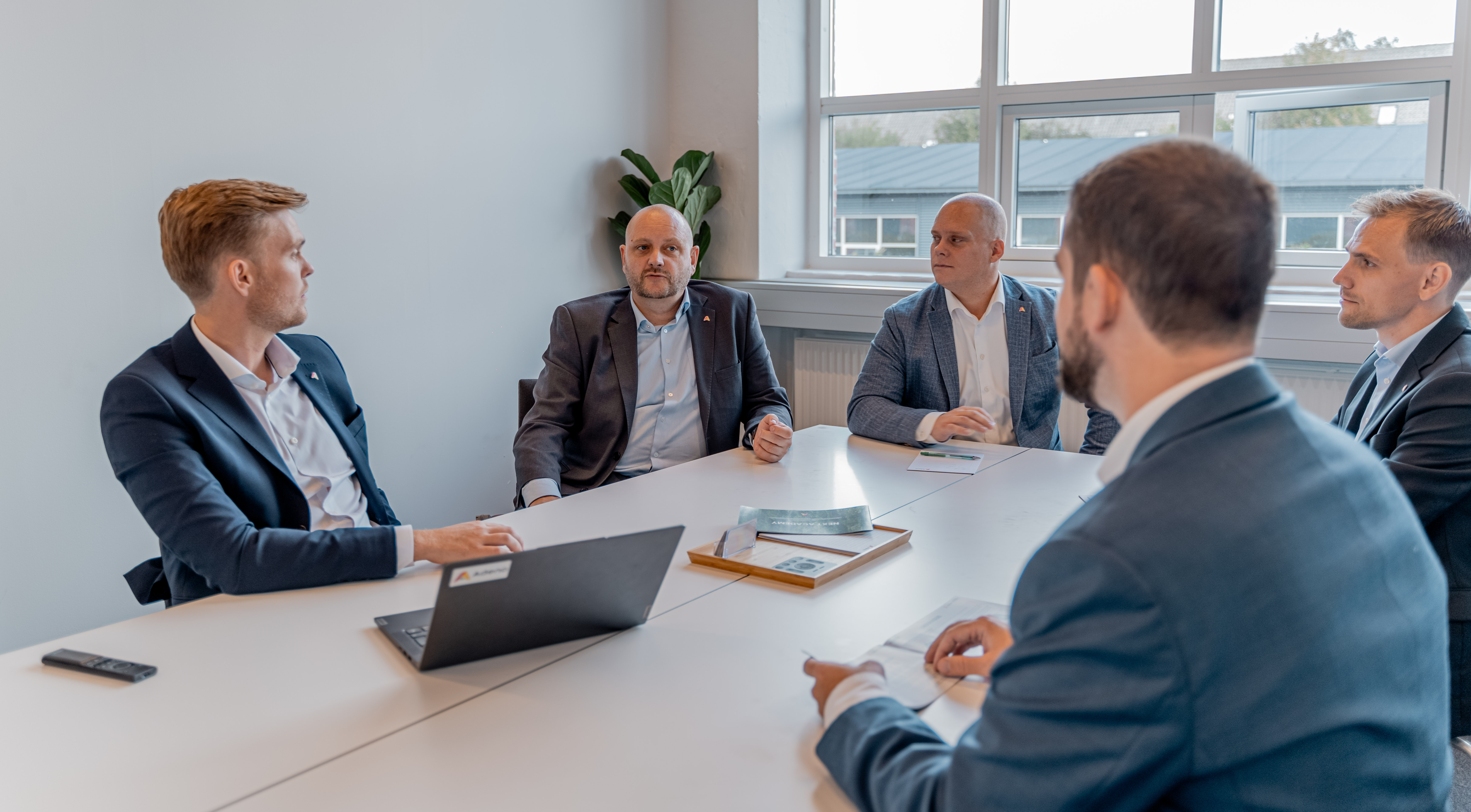 Five professionals in business attire sitting around a conference table at ServiceNow partner Adeno.