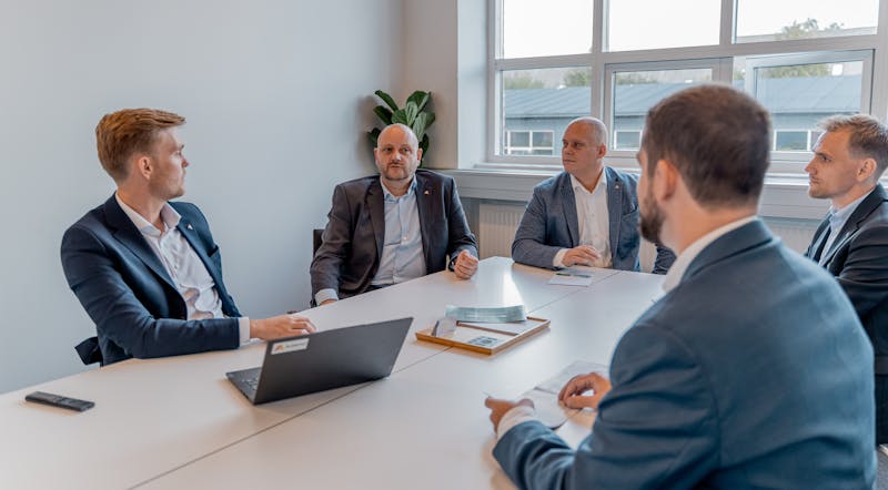 Five professionals in business attire sitting around a conference table at ServiceNow partner Adeno.