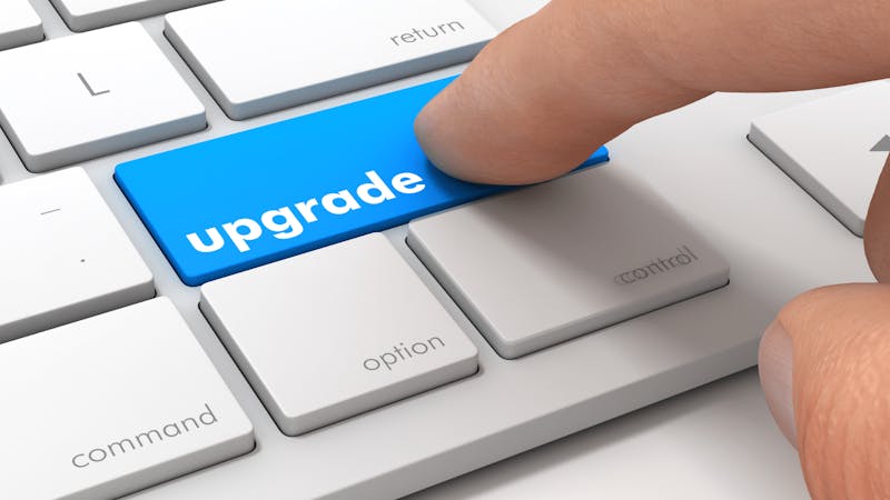 A finger pressing a blue upgrade key on a keyboard for a ServiceNow platform upgrade.