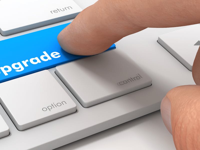 A finger pressing a blue upgrade key on a keyboard for a ServiceNow platform upgrade.