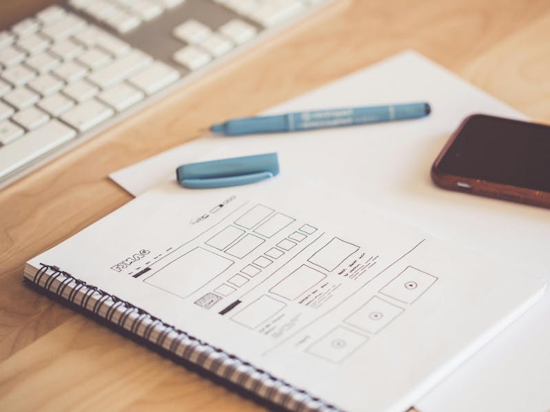 A desk with a keyboard, smartphone, and a notebook showing a hand-drawn ServiceNow UI wireframe.
