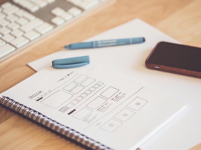 A desk with a keyboard, smartphone, and a notebook showing a hand-drawn ServiceNow UI wireframe.