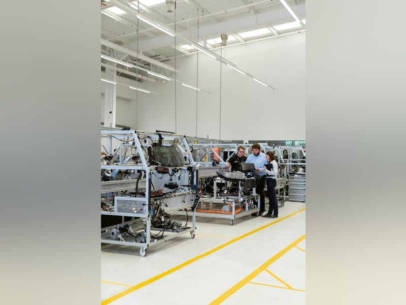 Three people in an industrial facility using a laptop near automotive testing rigs, illustrating ServiceNow.