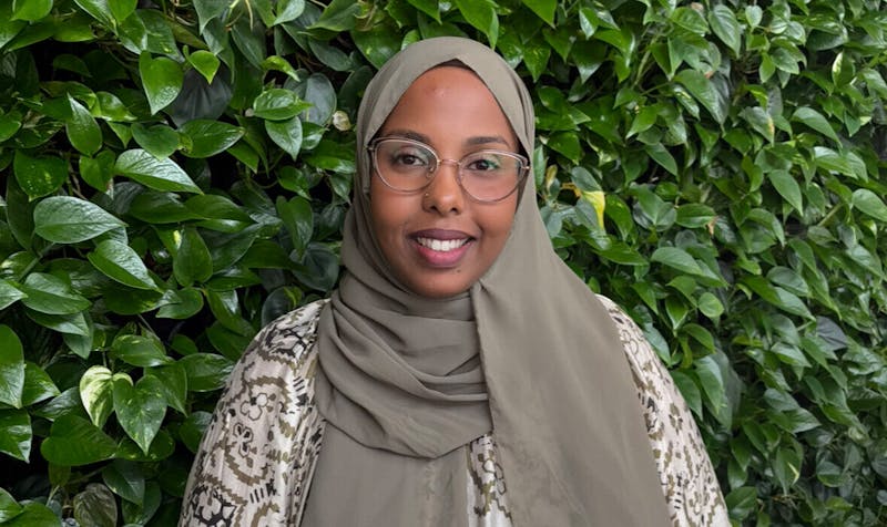 Portrait of Muna Ahmed Mohamed, a ServiceNow consultant, smiling in front of a wall of green plants.