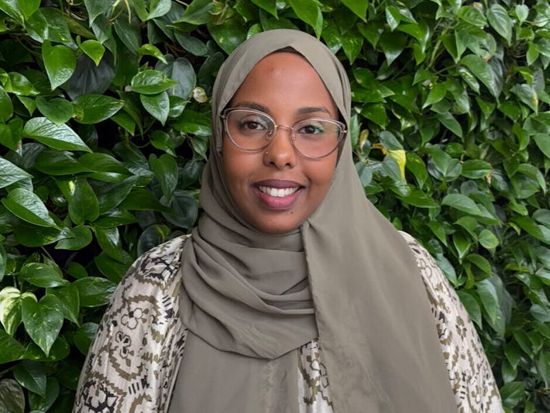Portrait of Muna Ahmed Mohamed, a ServiceNow consultant, smiling in front of a wall of green plants.