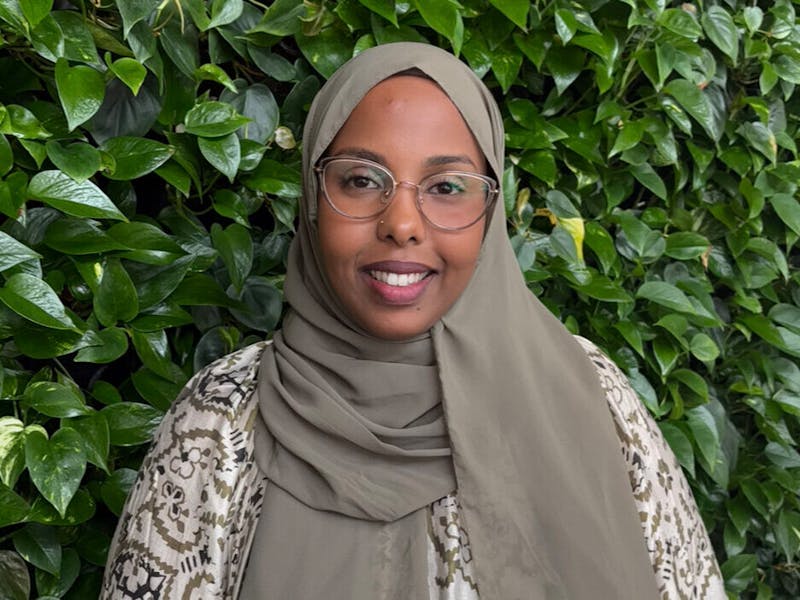 Portrait of Muna Ahmed Mohamed, a ServiceNow consultant, smiling in front of a wall of green plants.