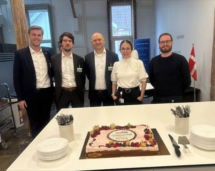 Five people standing behind a table with a cake celebrating the ServiceNow CSM go-live at Conscia.