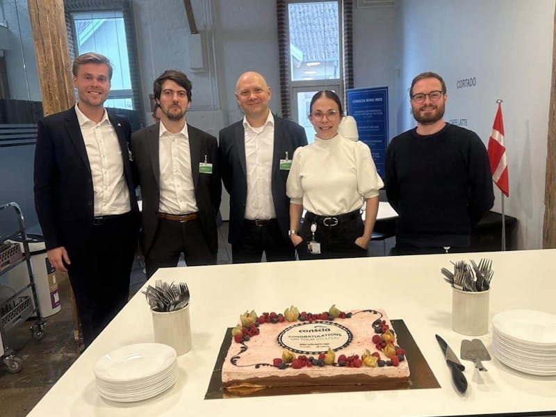Five people standing behind a table with a cake celebrating the ServiceNow CSM go-live at Conscia.