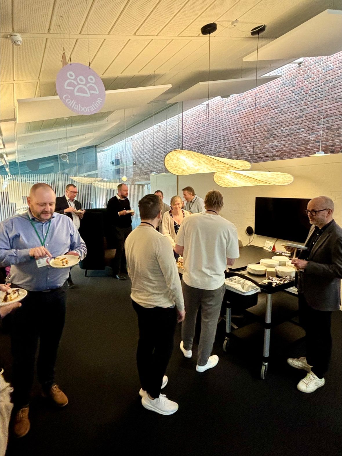 A group of people in an office celebrating a ServiceNow CMDB and CSDM go-live event with cake.