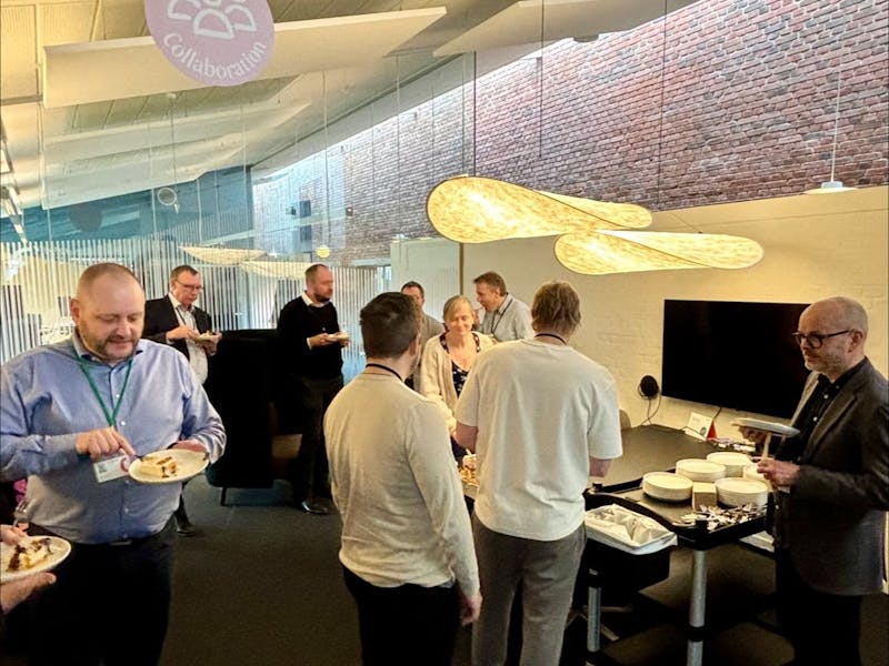 A group of people in an office celebrating a ServiceNow CMDB and CSDM go-live event with cake.