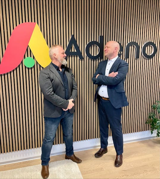 Two men standing in front of the Adeno logo at the new Silkeborg office of ServiceNow partner Adeno.