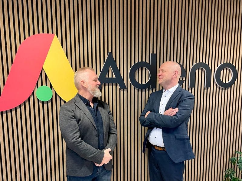 Two men standing in front of the Adeno logo at the new Silkeborg office of ServiceNow partner Adeno.