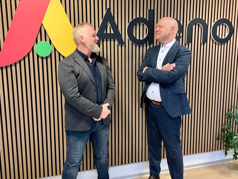 Two men standing in front of the Adeno logo at the new Silkeborg office of ServiceNow partner Adeno.