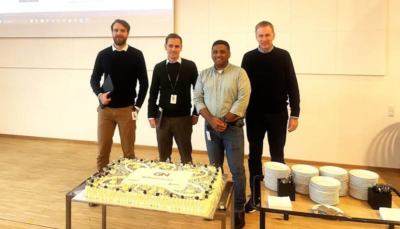 Four men standing behind a large cake celebrating a ServiceNow go-live at GN Store Nord.