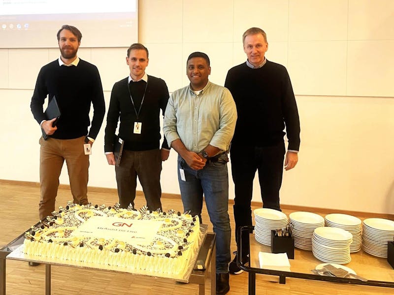 Four men standing behind a large cake celebrating a ServiceNow go-live at GN Store Nord.