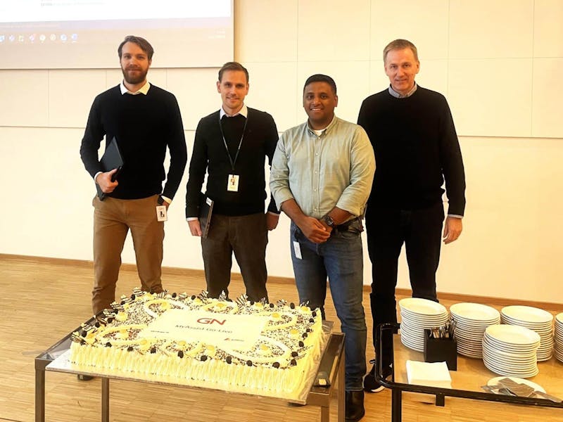 Four men standing behind a large cake celebrating a ServiceNow go-live at GN Store Nord.