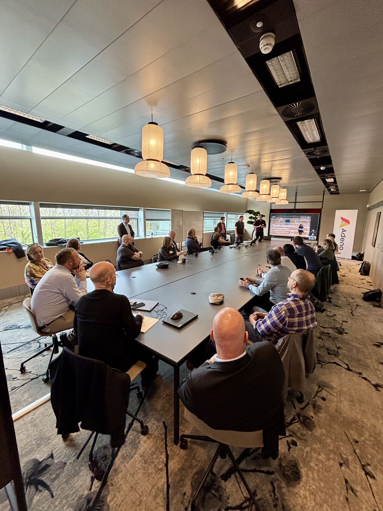 Professionals at a networking event and presentation in a modern conference room hosted by Adeno, a ServiceNow partner.