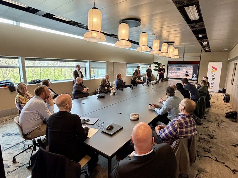Professionals at a networking event and presentation in a modern conference room hosted by Adeno, a ServiceNow partner.
