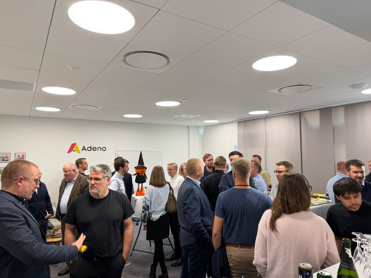 A group of people socializing in an office setting at a housewarming event for ServiceNow Partner Adeno.