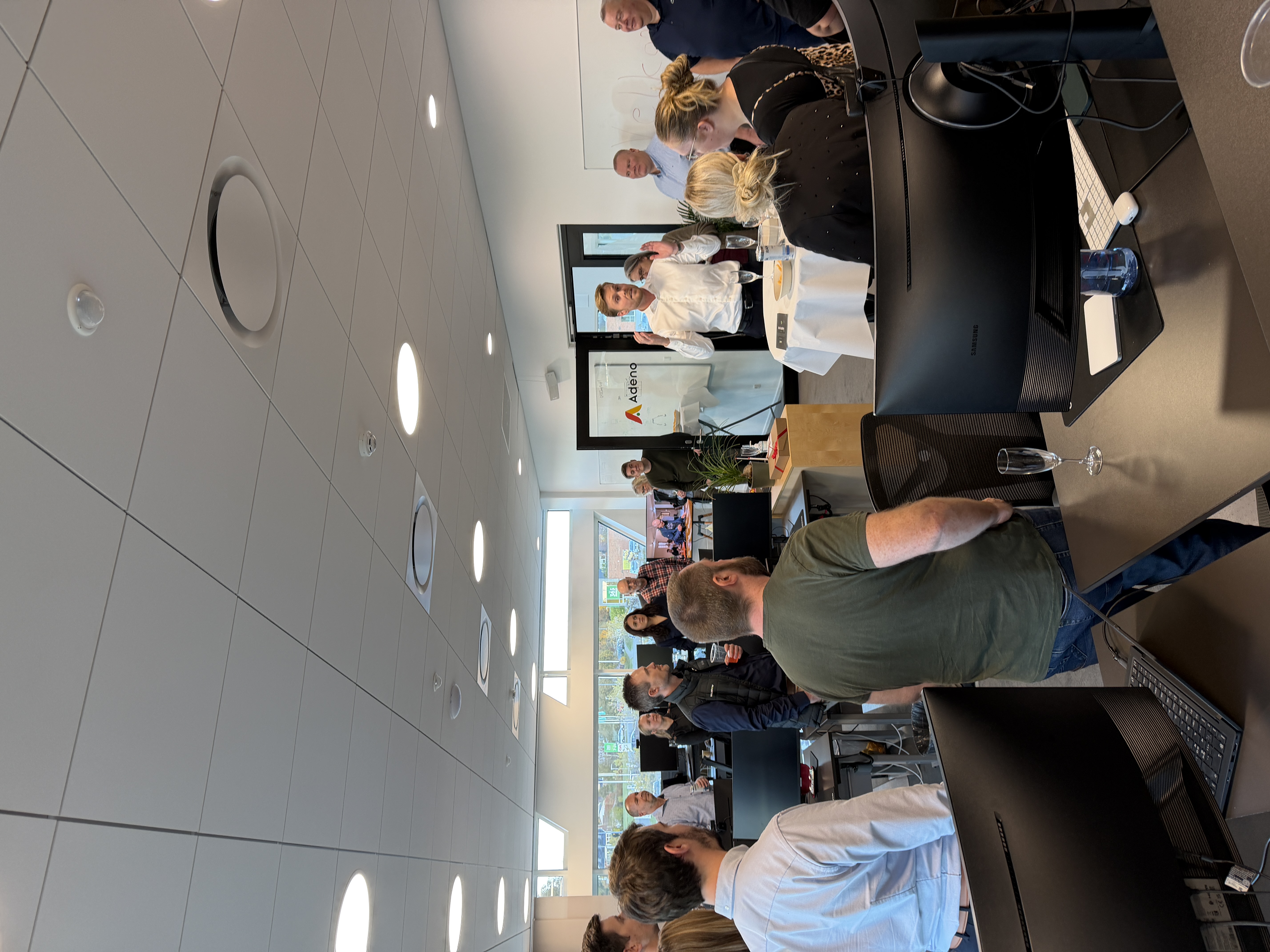 A group of people gathered in an office for a housewarming event at Adeno, a ServiceNow partner.