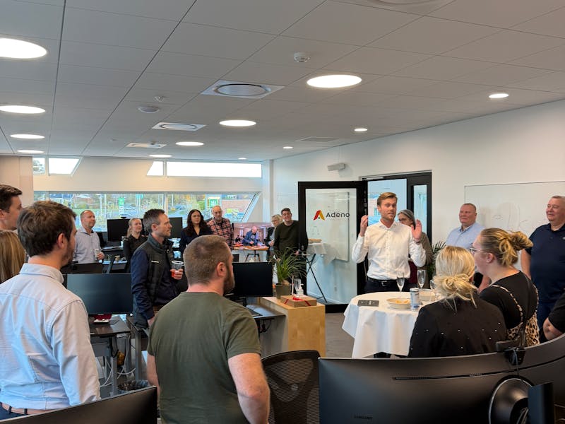 A group of people gathered in an office for a housewarming event at Adeno, a ServiceNow partner.