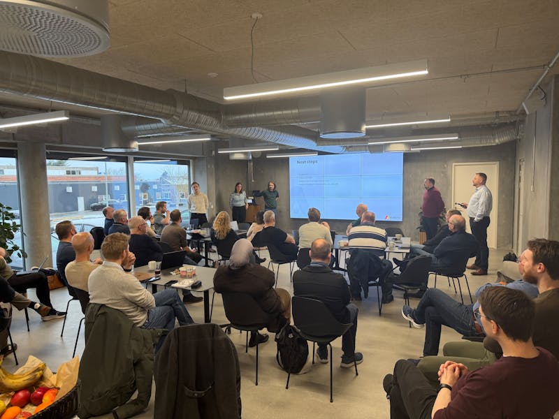 A group of people attending a ServiceNow hackathon presentation with a screen displaying project updates.