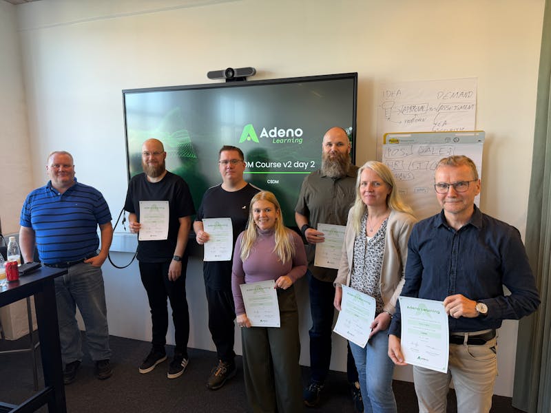 A group of people holding certificates in front of a screen for a ServiceNow CSDM course.