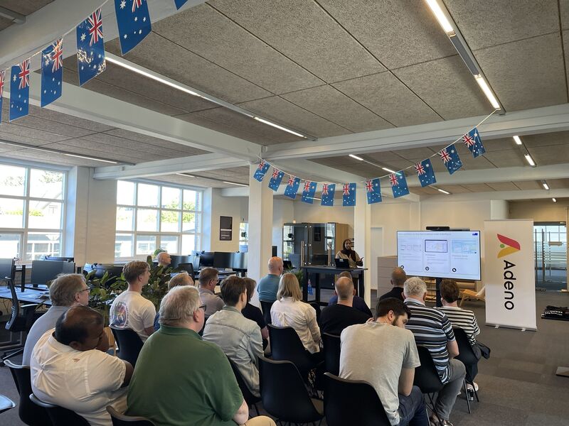 People attending a ServiceNow Australia Release Event presentation in an office with Australian flags and an Adeno banner.