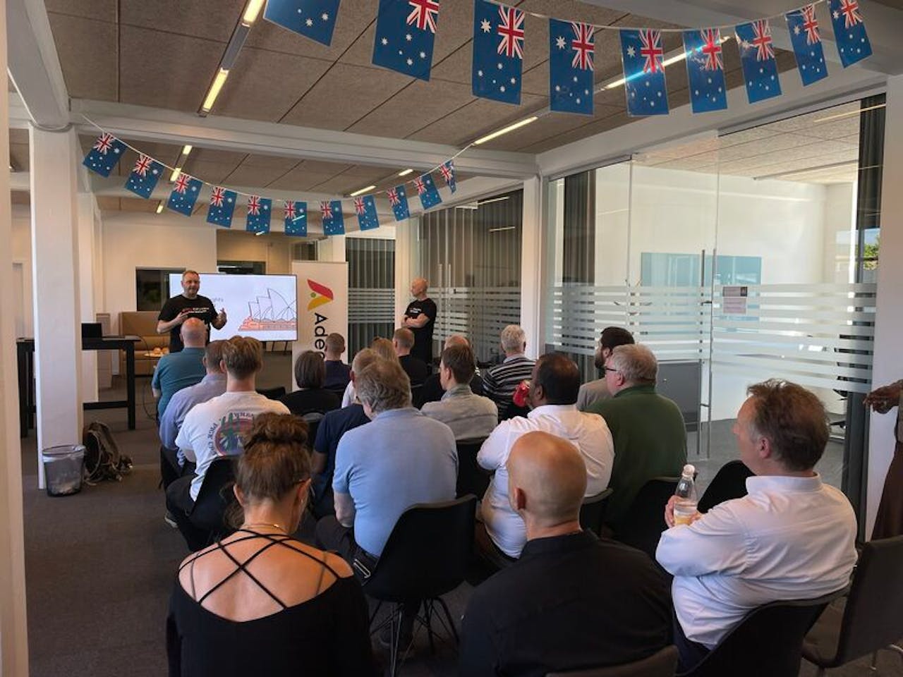People attending a ServiceNow Australia Release Event presentation in an office decorated with Australian flags.