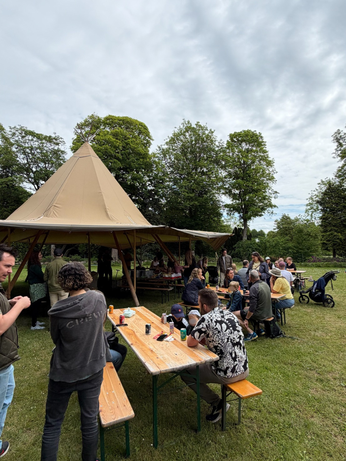 People gathered at picnic tables near a tipi tent for an Adeno family day event, a ServiceNow partner.