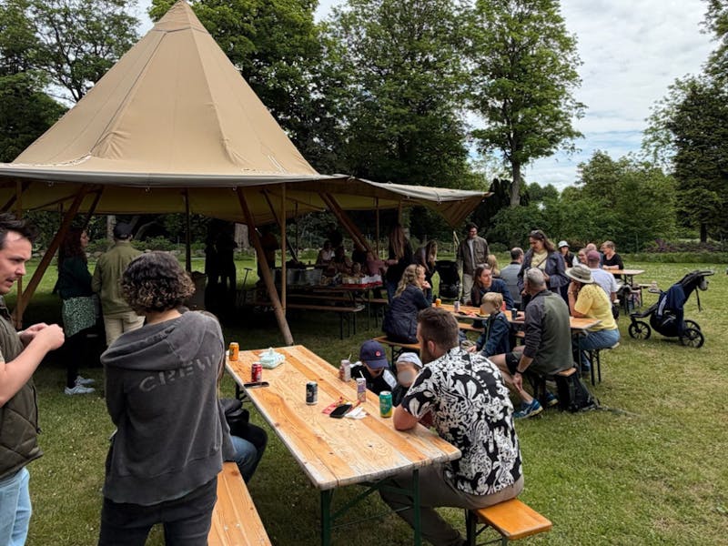 People gathered at picnic tables near a tipi tent for an Adeno family day event, a ServiceNow partner.