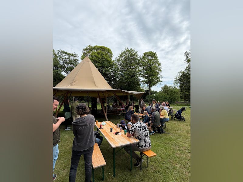 People gathered at picnic tables near a tipi tent for an Adeno family day event, a ServiceNow partner.