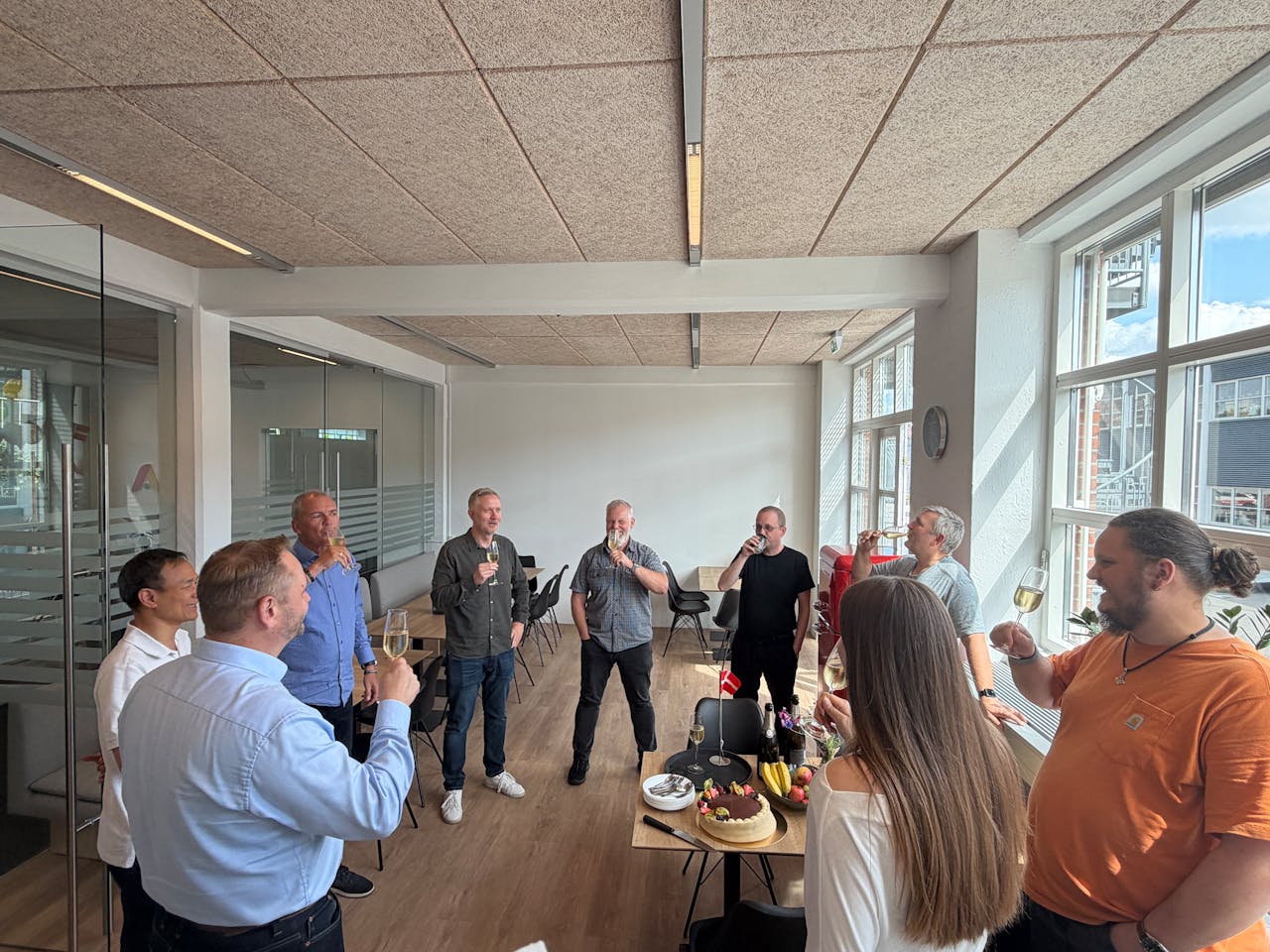 A group of people celebrating the ServiceNow Next Academy graduation in an office setting with a toast and a cake.