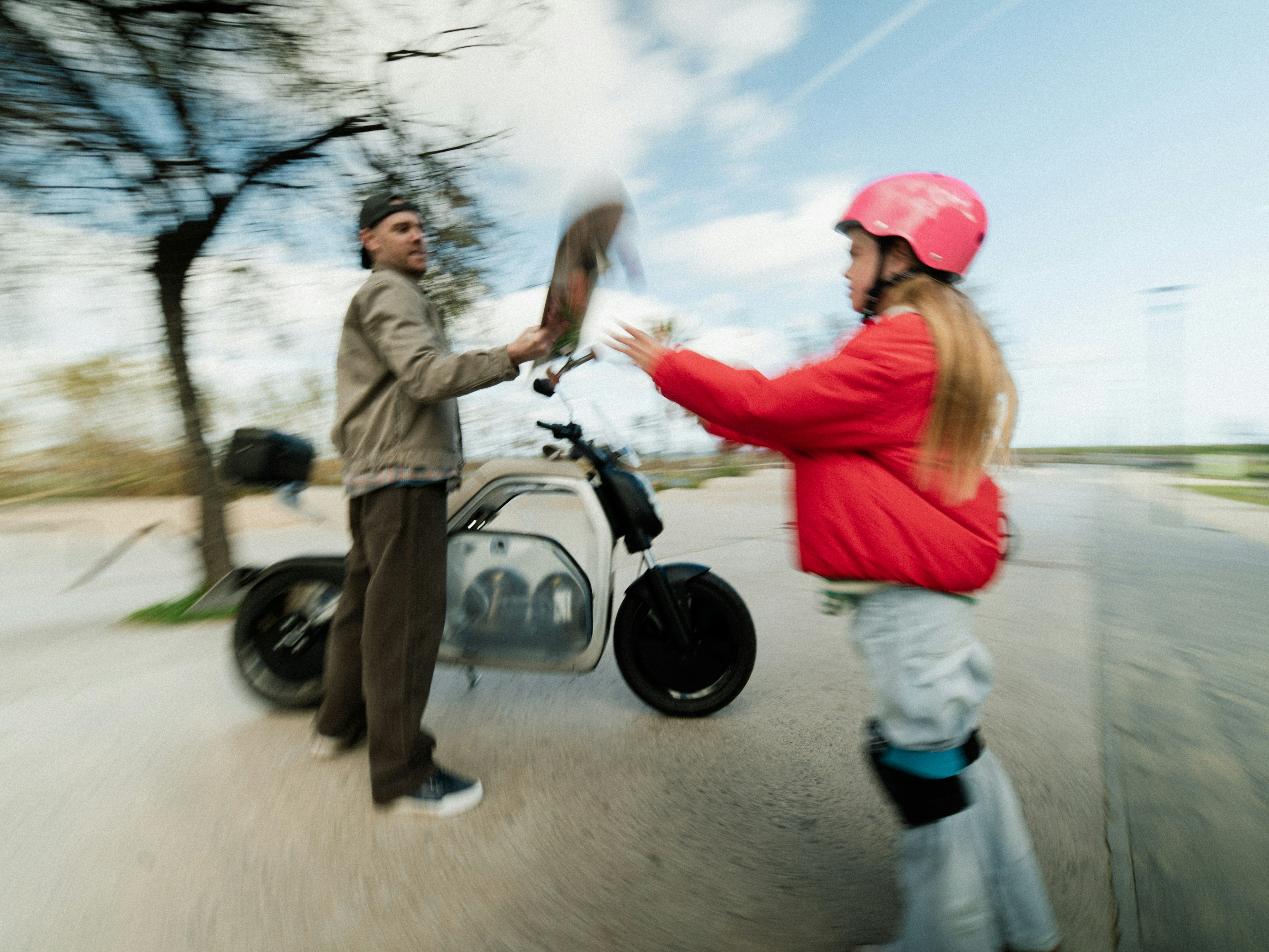 Child with helmet high-fives a person beside an electric bike on a tree-lined road.