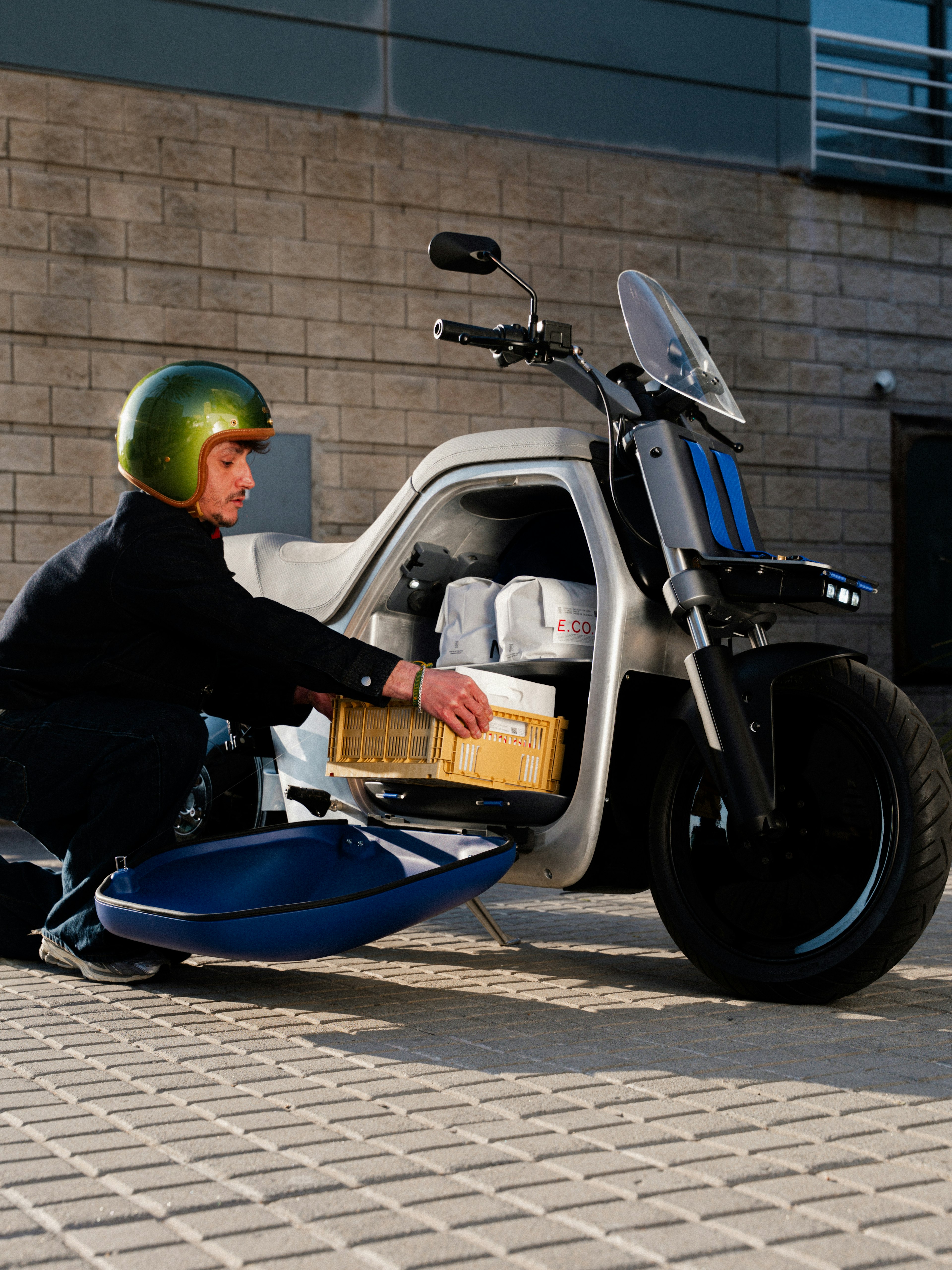 Una persona que carga un paquete en el maletero de una motocicleta de carga moderna mientras lleva un casco verde.