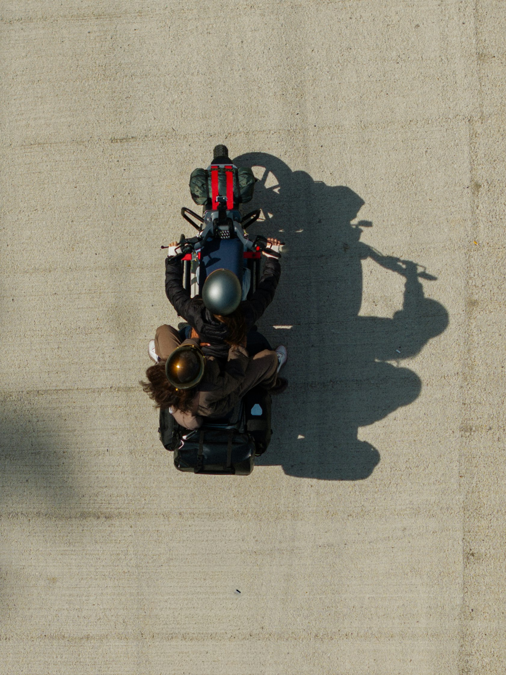 Vista aerea di una persona in sella a una moto su una superficie di cemento, che proietta un'ombra a destra.