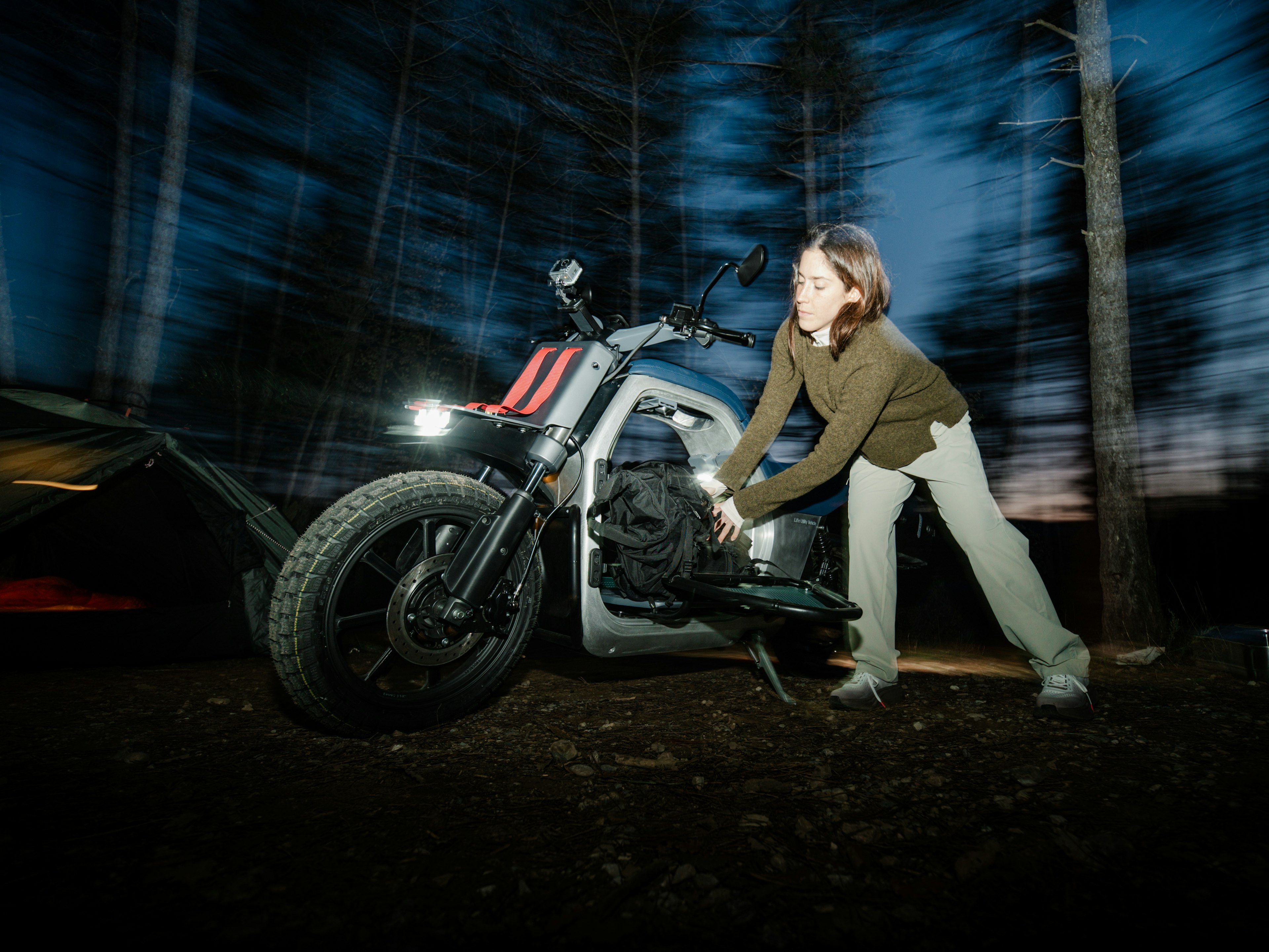 Una persona che spinge una moto al tramonto in un'area boschiva.
